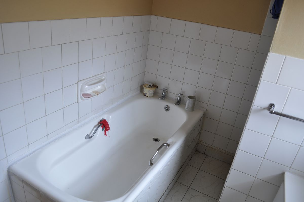 A functional bathroom featuring a built-in bathtub with chrome fixtures and white ceramic wall and floor tiling.