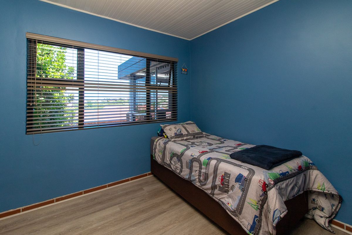 A bedroom featuring blue painted walls, laminate flooring, a tongue and groove ceiling, and an aluminium window with fitted venetian blinds.