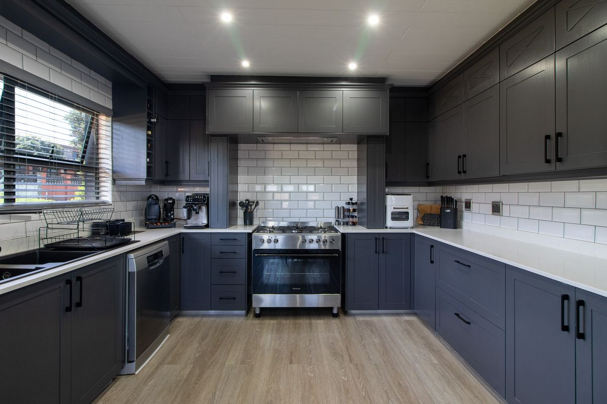 Modern kitchen featuring dark grey shaker cabinetry, white subway tile backsplash, quartz countertops, and a stainless steel gas stove.