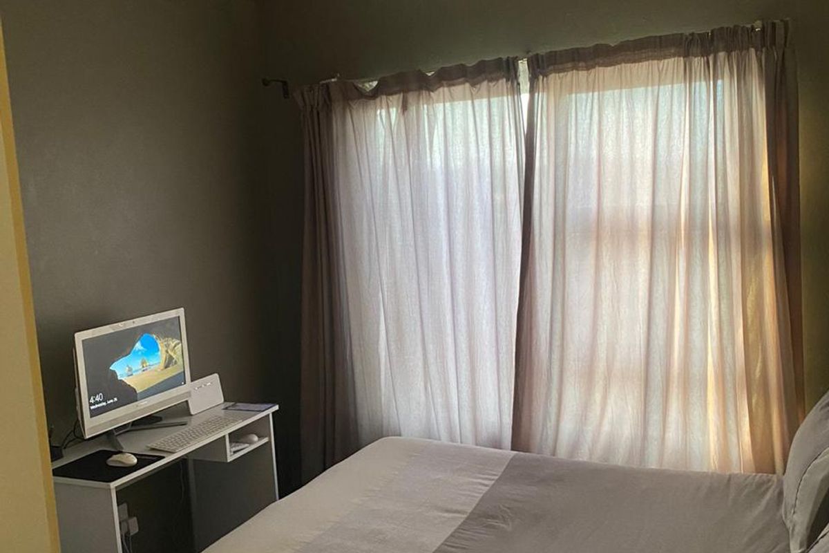 A bedroom featuring dark walls and a window with curtains, showing visible signs of water damage on the ceiling.