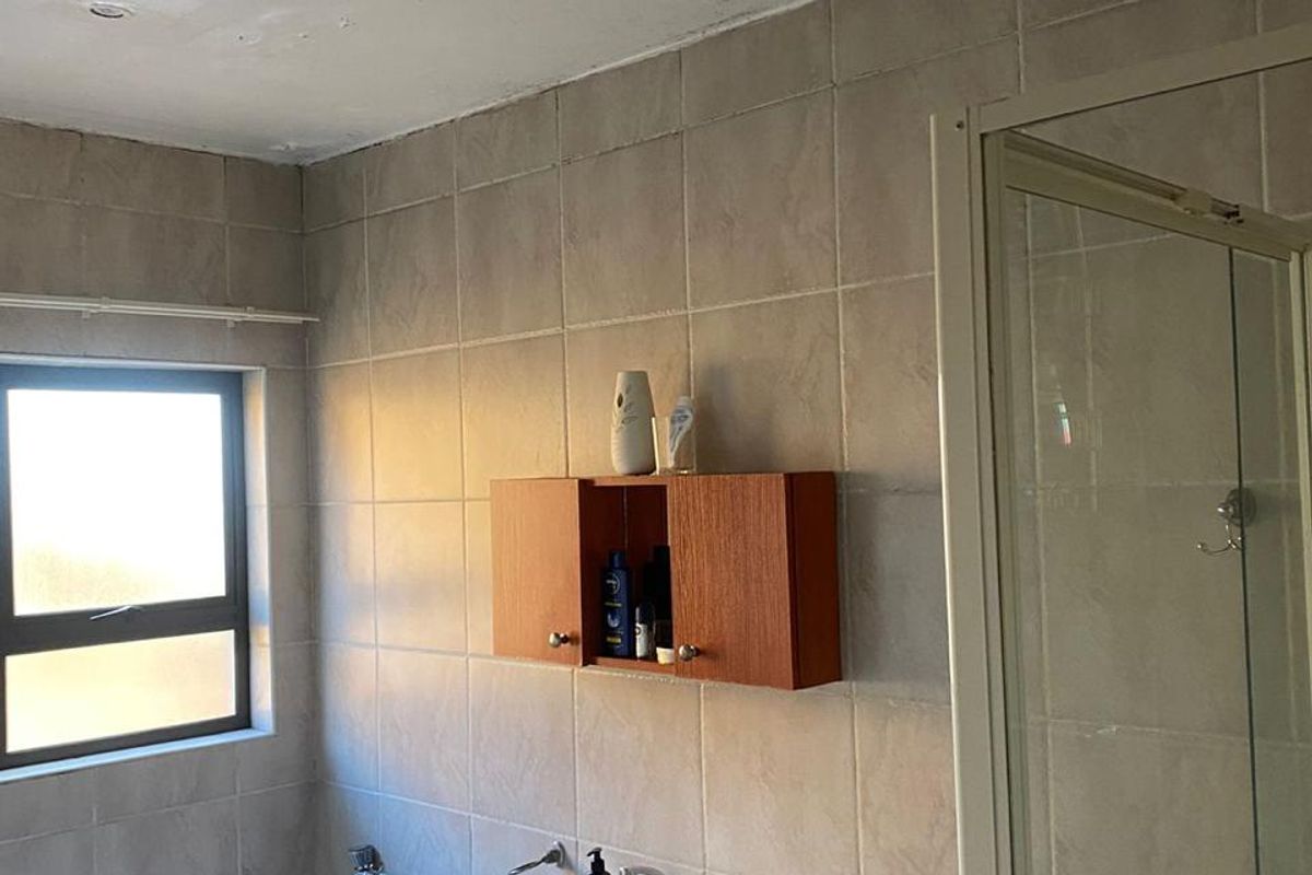 Bathroom featuring a pedestal basin, bathtub, and separate shower enclosure with tiled walls. The ceiling requires maintenance and repainting.