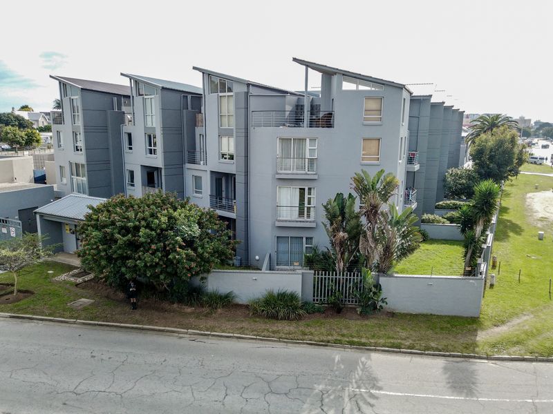 An aerial view of a modern multi-story apartment complex featuring grey facades, private balconies, and a secure perimeter wall with landscaped garden areas.