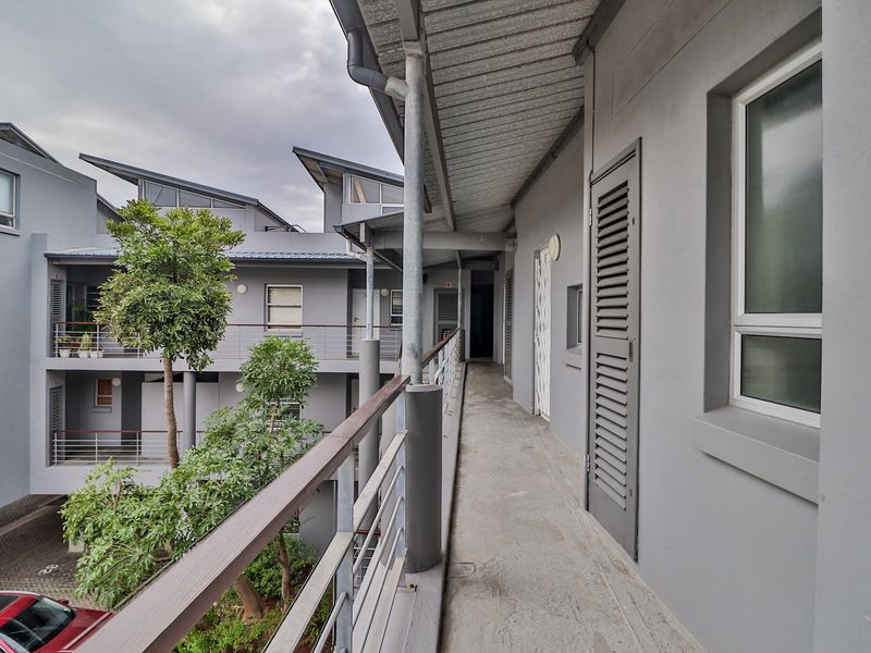 An exterior walkway balcony featuring concrete flooring, metal railings, and louvered doors, overlooking the apartment complex courtyard.