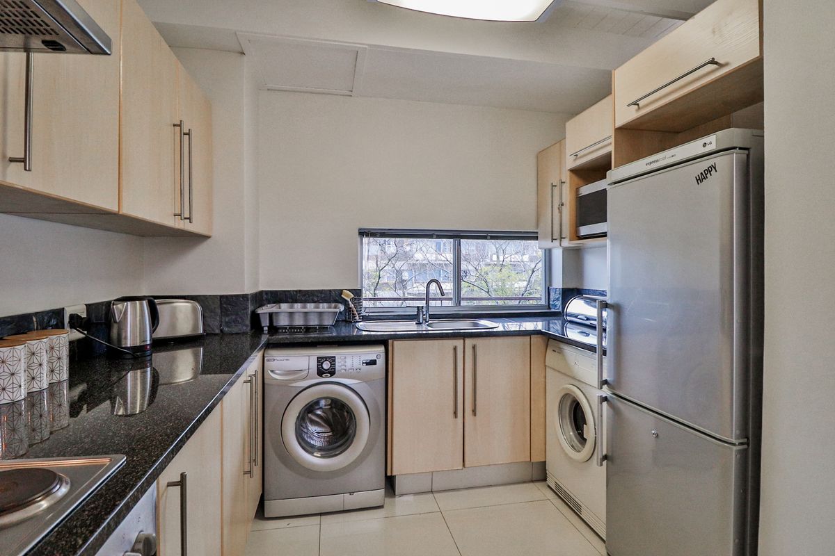 Compact kitchen featuring light wood cabinetry, granite countertops, integrated appliances, and tiled flooring with a functional layout.