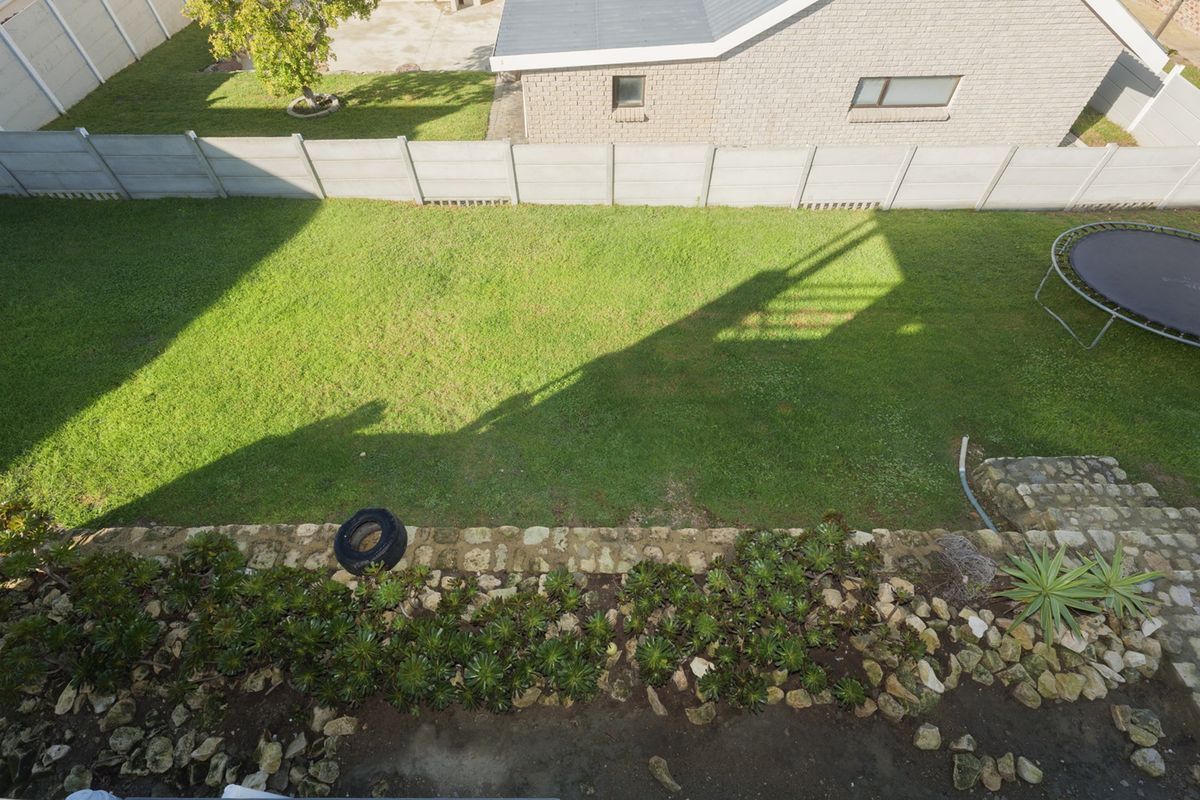 An elevated view of a private rear garden featuring a lawn, stone retaining wall, and secure precast concrete boundary walling.