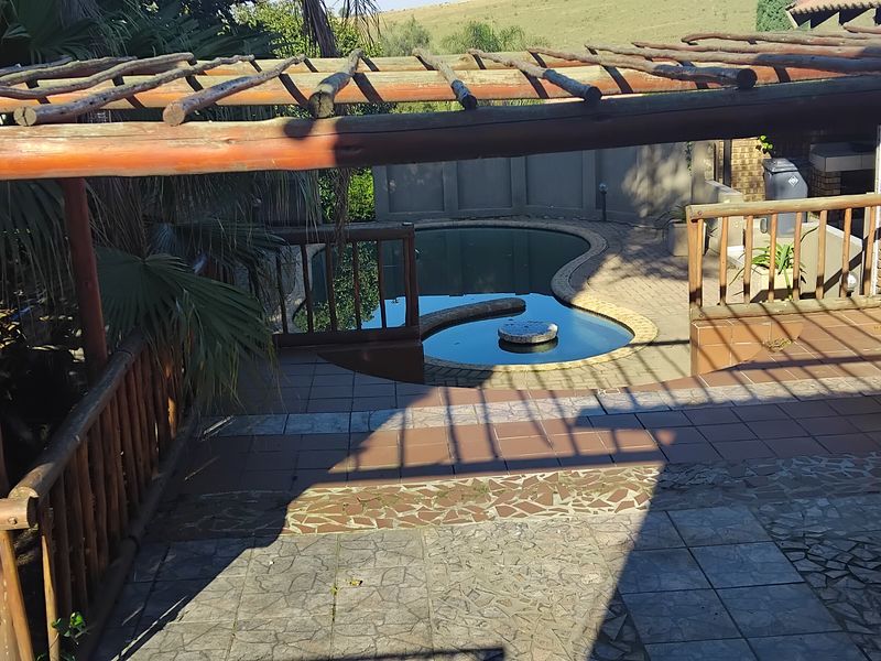 Outdoor pool area featuring a tiled patio, wooden pergola structure, and a kidney-shaped swimming pool with a built-in water feature.