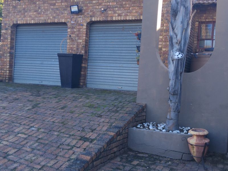 Front exterior view of the property featuring a double garage, brick facade, and paved driveway with established landscaping.