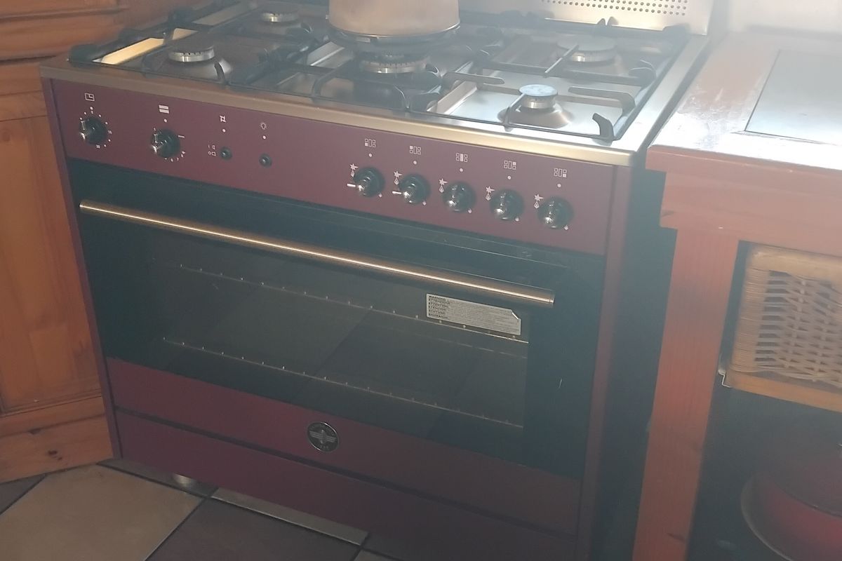 A kitchen area featuring a prominent maroon gas stove and oven unit set within traditional wooden cabinetry and tiled flooring.