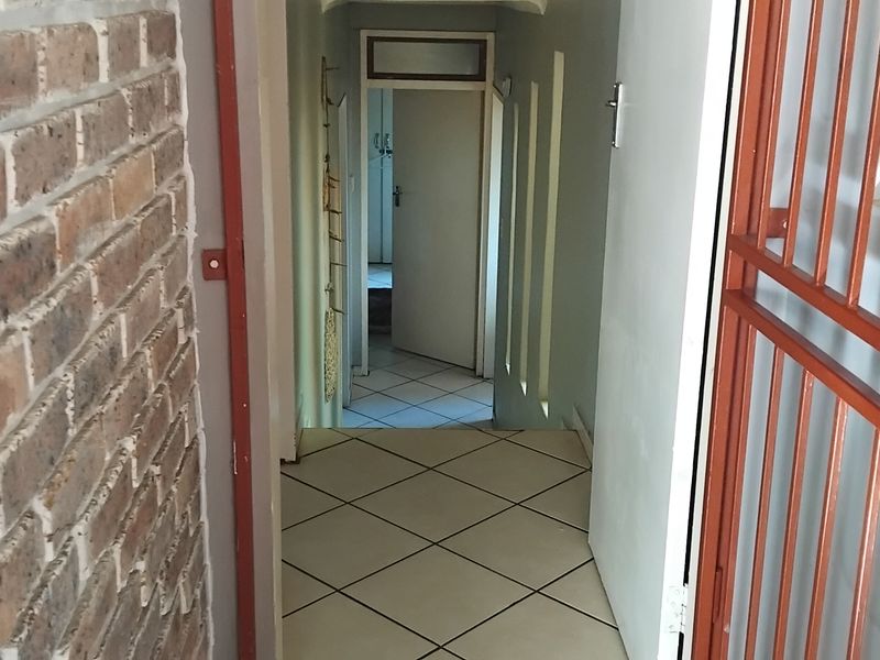 A functional hallway featuring tiled flooring, an exposed brick feature wall, and a metal security gate leading to internal rooms.