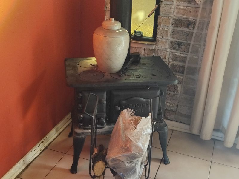 A living area featuring a vintage cast iron wood burning stove set against a brick fireplace surround with tiled flooring.
