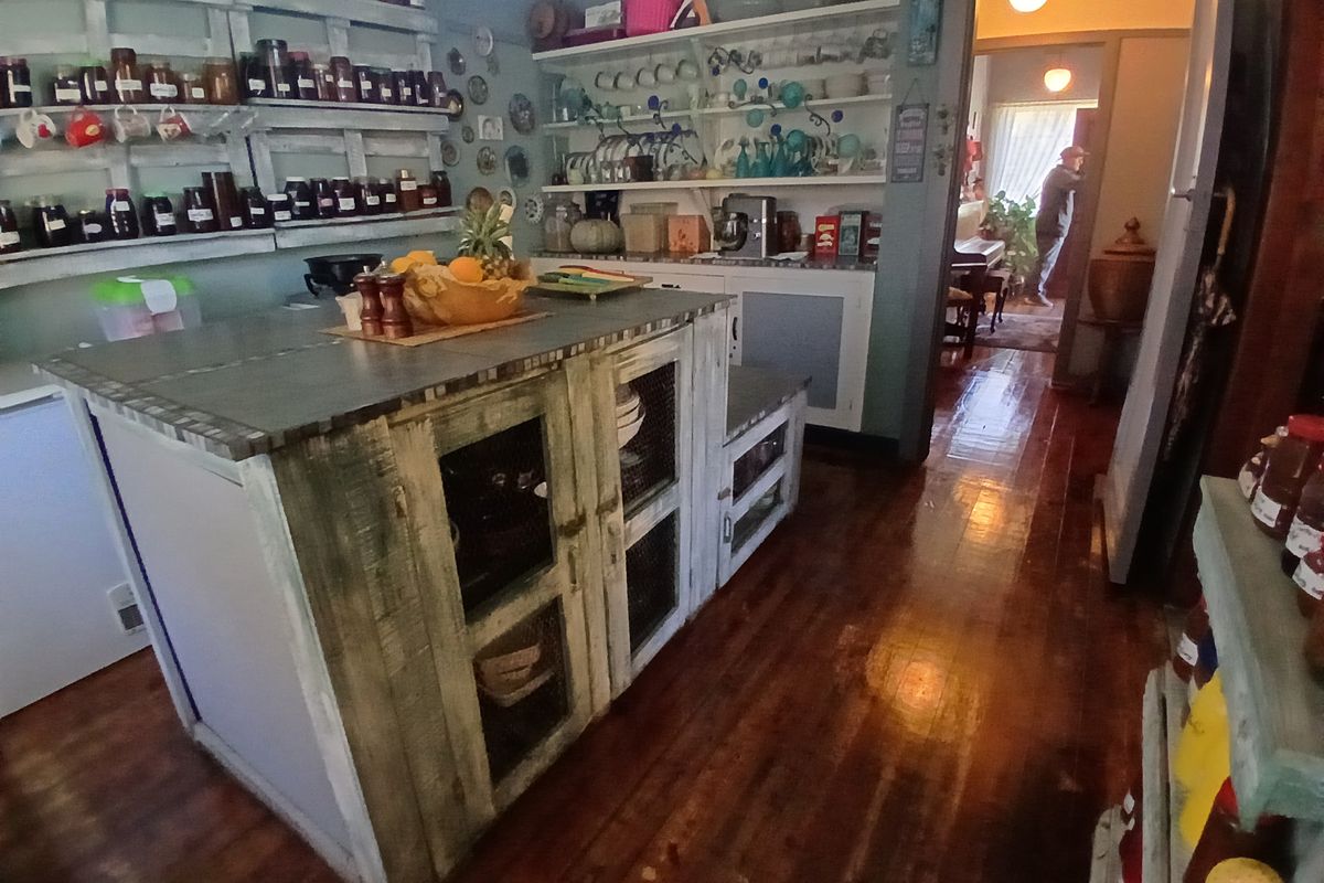 A rustic-style kitchen featuring a central island, extensive open shelving, and polished hardwood flooring, leading into an adjacent living area.