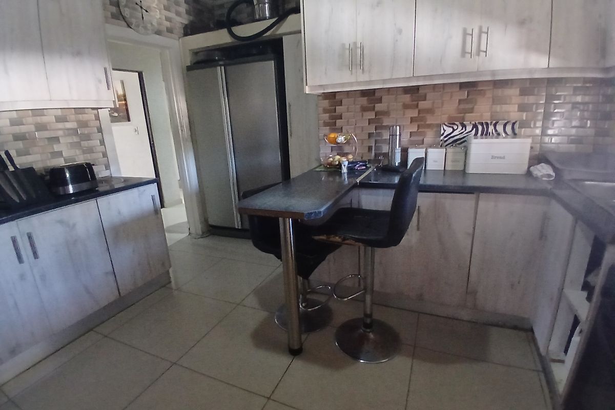 A functional kitchen featuring light wood-look cabinetry, tiled backsplash, and a built-in breakfast bar with tiled flooring.