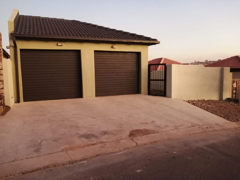 A double garage with roller doors and a concrete driveway, featuring a perimeter wall and pedestrian gate access.