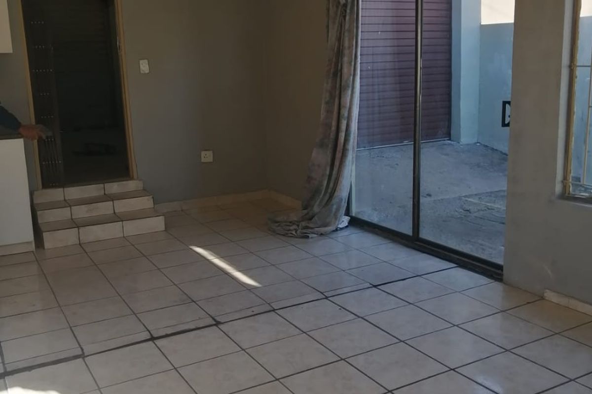 An empty living room featuring ceramic tiled flooring, a sliding glass door leading to the exterior, and a stepped entrance to an adjacent room.