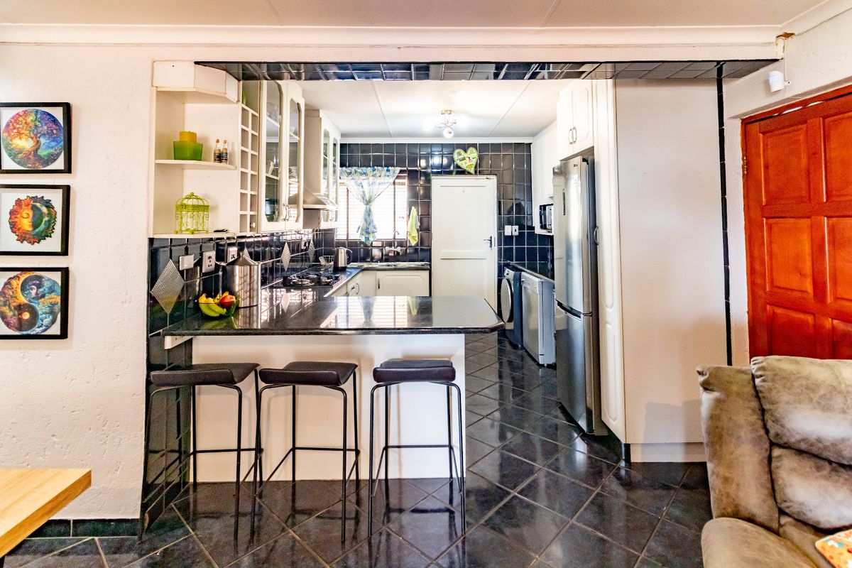 A functional kitchen featuring dark tiled flooring, granite countertops, a breakfast bar, and ample built-in cabinetry with a contrasting tiled backsplash.