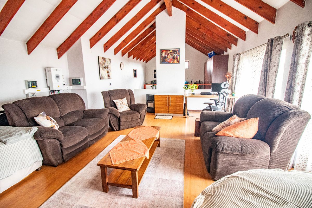 Spacious living area featuring a high vaulted ceiling with exposed timber rafters and warm laminate flooring, creating an open and airy atmosphere.