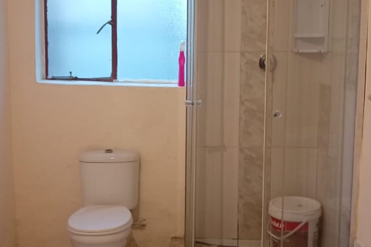 A functional bathroom featuring a corner shower enclosure, toilet, and tiled flooring. The space requires cosmetic updates and maintenance to improve its overall condition.
