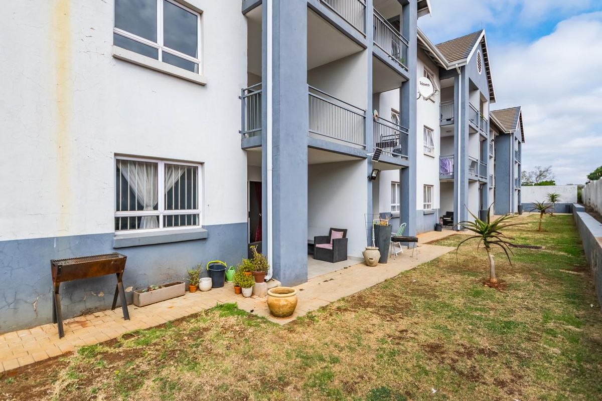 Rear view of an apartment complex featuring ground-floor patios, upper-level balconies, and a shared garden area with paved walkways.