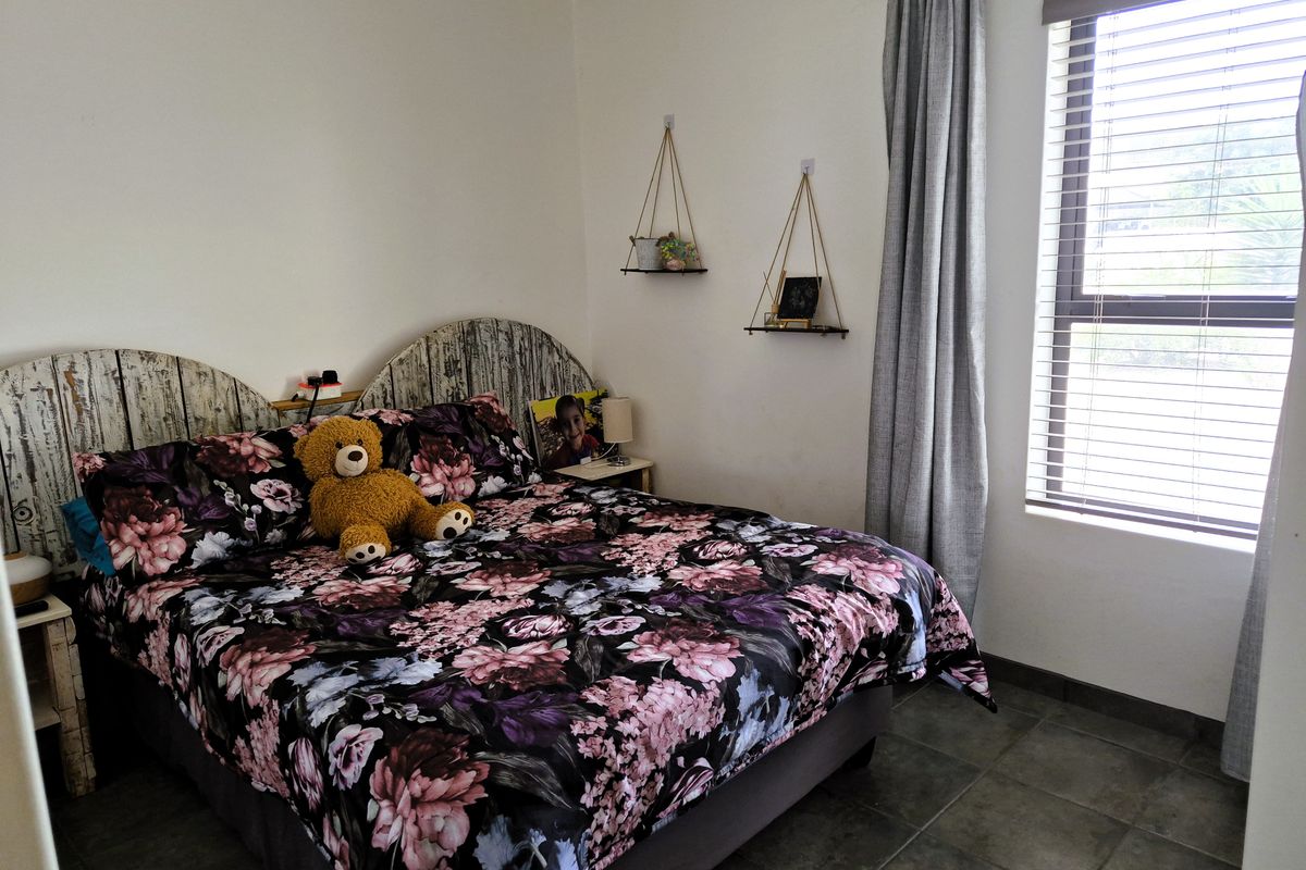 A functional bedroom featuring tiled flooring, a large window with venetian blinds, and neutral wall finishes.