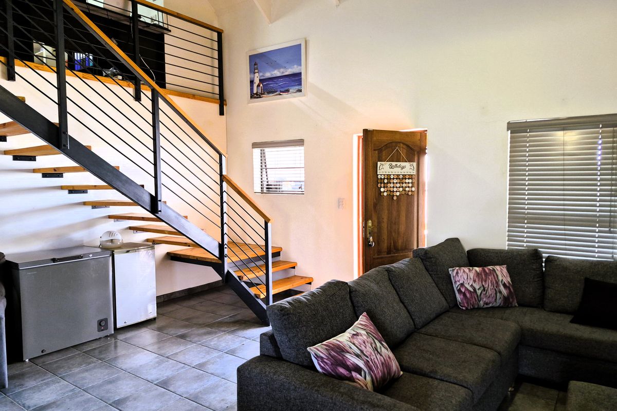 Open-plan living area featuring a modern staircase with metal balustrades, tiled flooring, and vaulted ceilings, providing a bright and airy atmosphere.