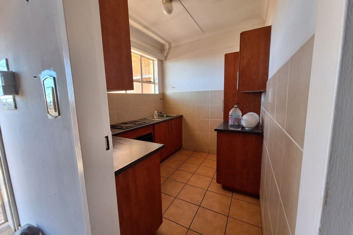 A compact kitchen featuring wooden cabinetry, laminate countertops, ceramic tile backsplash, and tiled flooring, offering a functional layout ready for modernization.