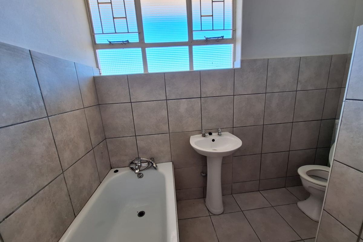 A functional bathroom featuring a bathtub, pedestal basin, and toilet with neutral wall and floor tiling.