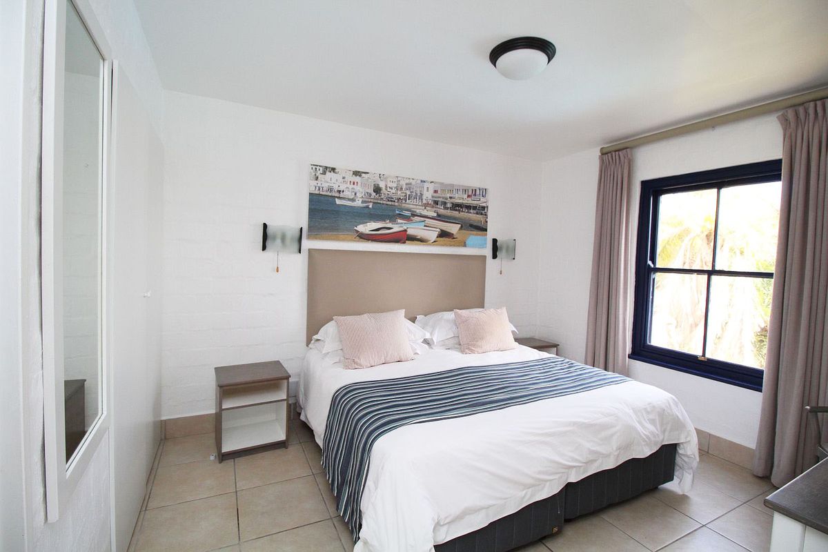 A bedroom featuring tiled flooring, a built-in cupboard with a mirror, and a window with curtains.