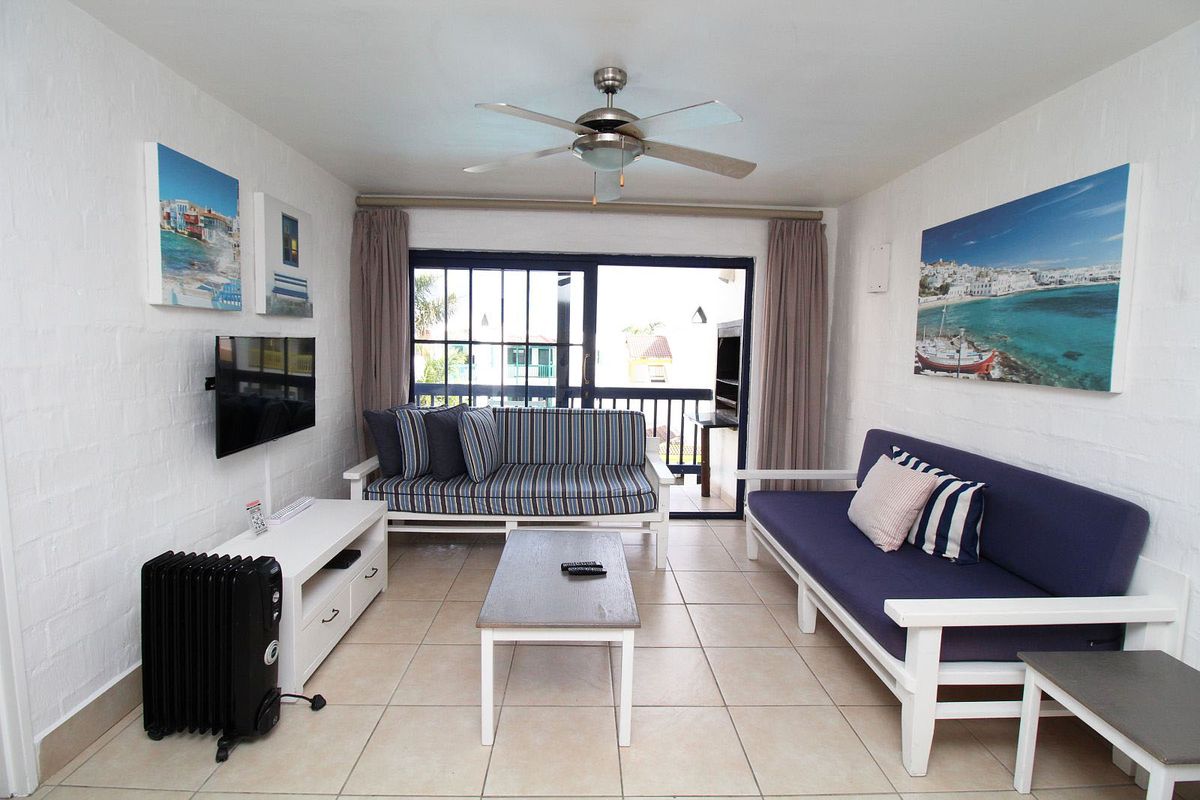 A bright living room featuring tiled flooring, a ceiling fan, and large sliding glass doors that open onto a private balcony.