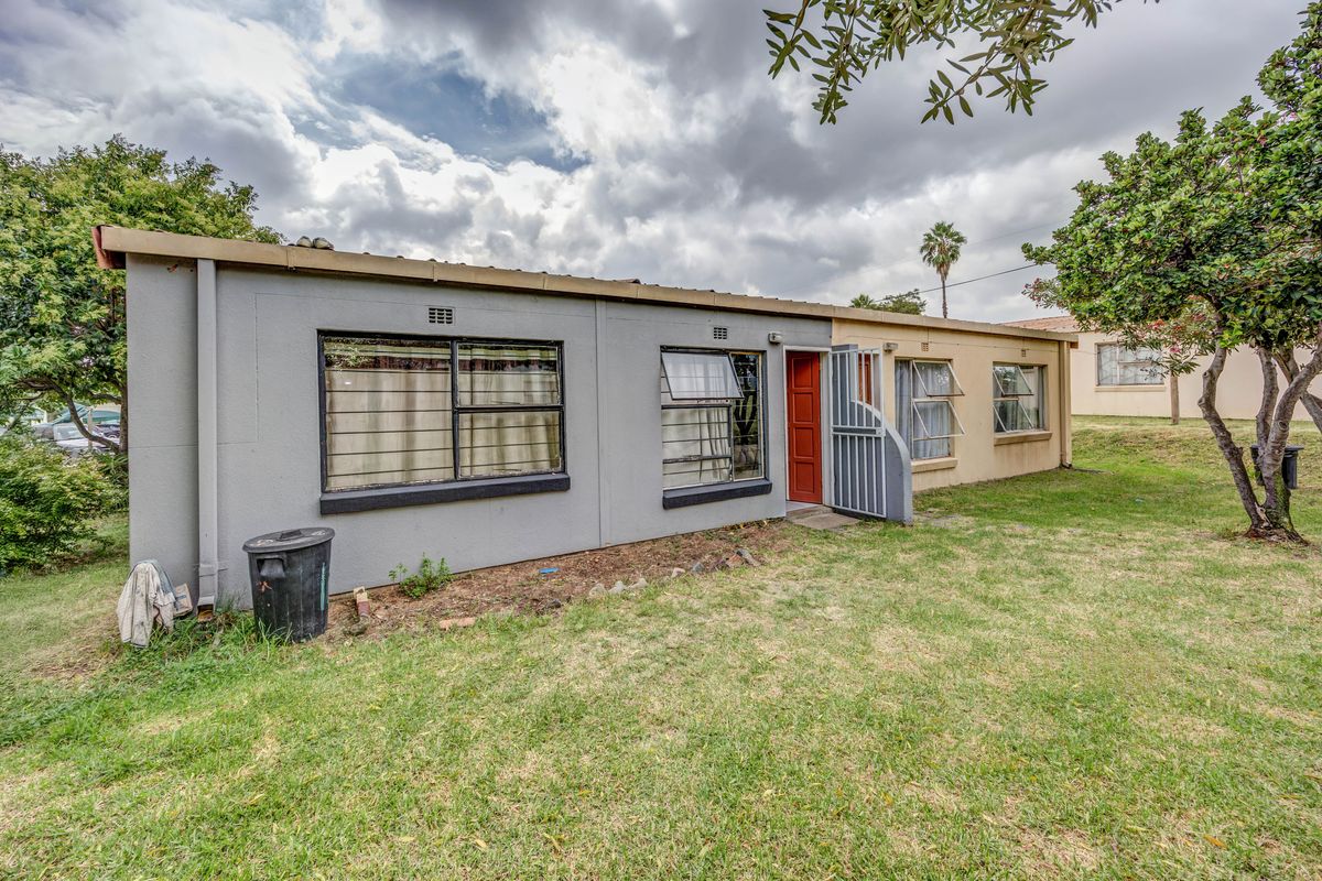 Rear view of the townhouse featuring a private garden area, metal security gate, and multiple window access points.