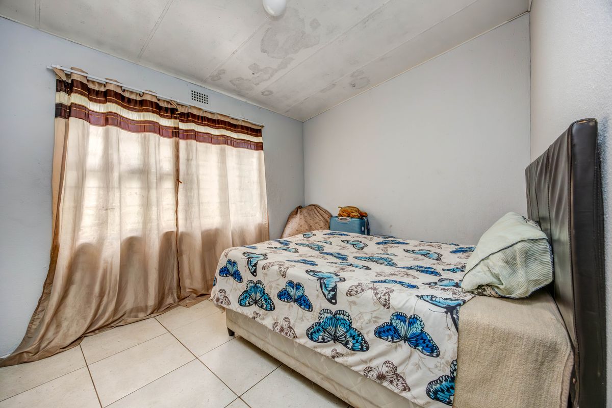 A bedroom featuring tiled flooring and a window with curtain tracks. The ceiling shows visible signs of water damage.