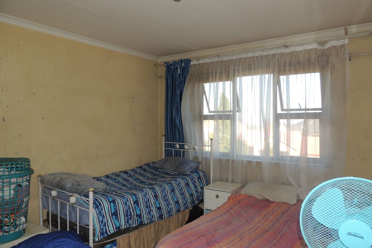 A bedroom featuring a window with curtain rails and worn wall finishes, requiring cosmetic updates to improve the overall aesthetic and condition.