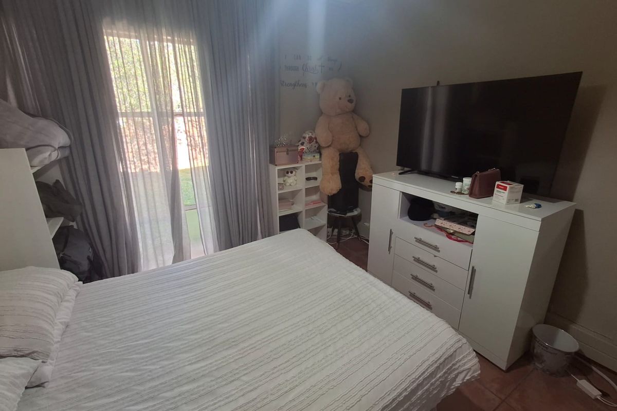 A bedroom featuring tiled flooring and large windows with curtains, providing natural light and a view of the exterior.