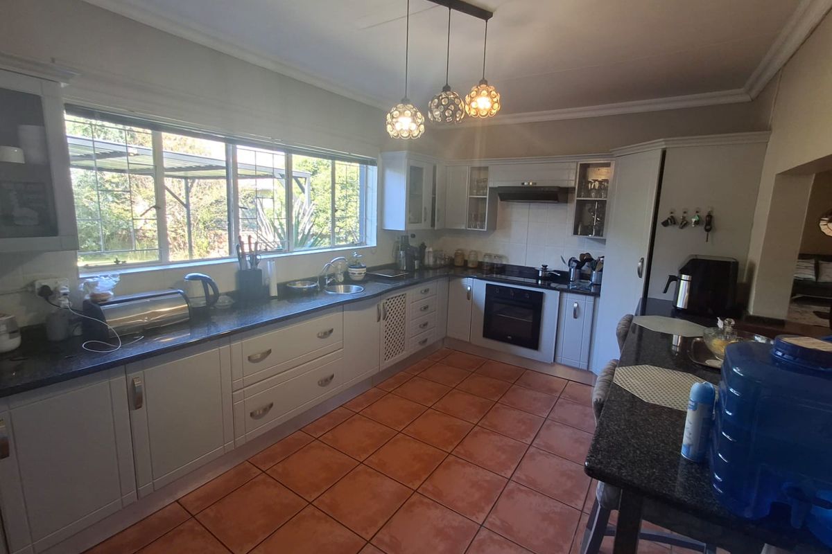 A functional kitchen featuring white cabinetry, dark granite countertops, integrated appliances, and terracotta floor tiles, offering a bright and practical workspace.