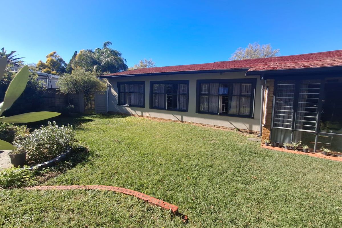 A view of the rear exterior of the house featuring a lawn, brick garden edging, and windows with security bars.
