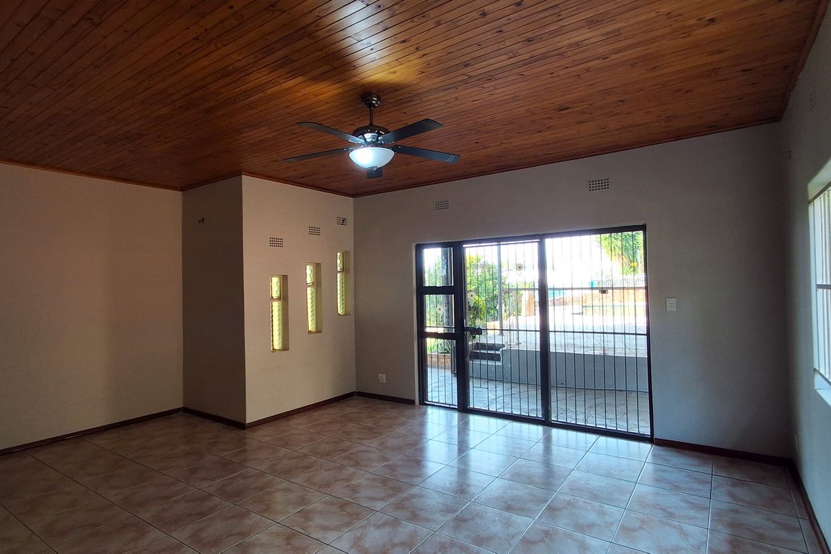 Spacious living area featuring a timber-clad ceiling, ceiling fan, tiled flooring, and large sliding glass doors with security gates leading to the exterior.
