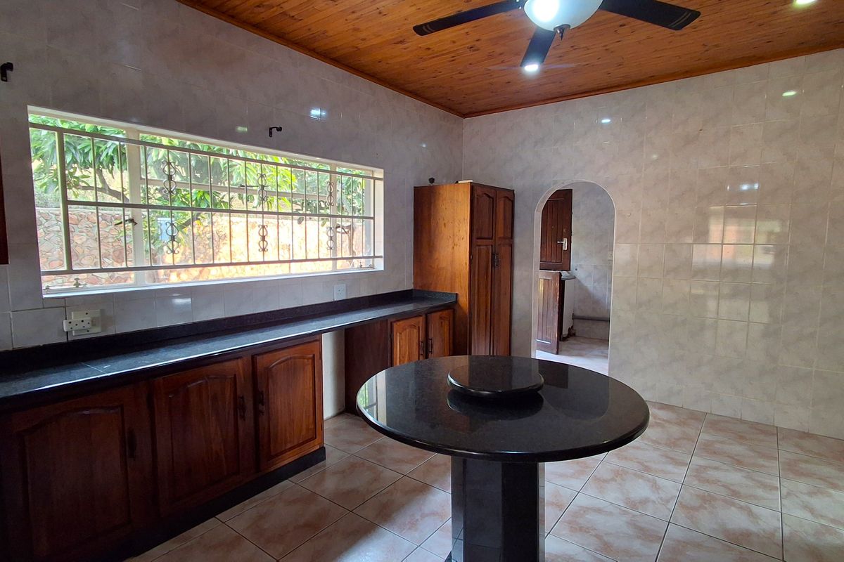 A functional kitchen featuring dark granite countertops, wooden cabinetry, tiled flooring, and a timber-clad ceiling with a central ceiling fan.