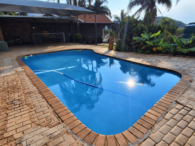 Outdoor pool area featuring a swimming pool with paved surround, covered patio space, and established garden landscaping.