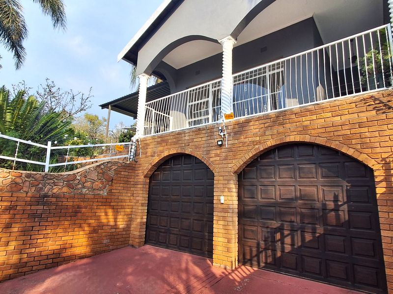 Exterior view of a double garage with brick facade and an upper-level balcony featuring white railings and arched architectural details.