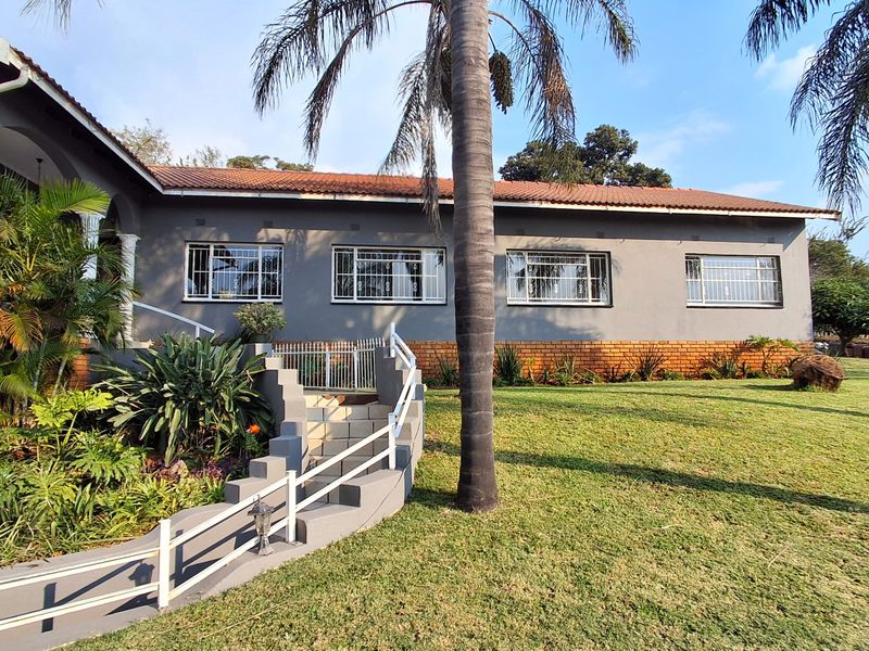 A view of the rear exterior of the house featuring a tiled roof, grey painted walls, brick base, and a landscaped garden with stairs.
