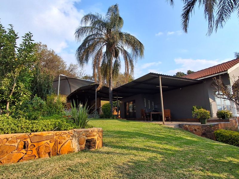 A spacious rear garden featuring a covered patio area, stone retaining walls, and established landscaping, providing an ideal space for outdoor relaxation and entertainment.