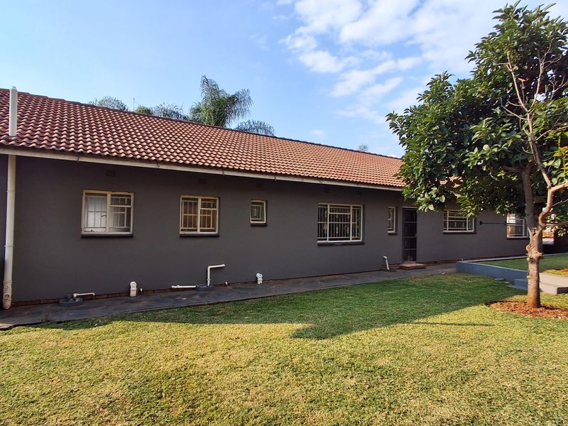 A view of the rear exterior of the house featuring a tiled roof, dark grey painted walls, and a well-maintained lawn.