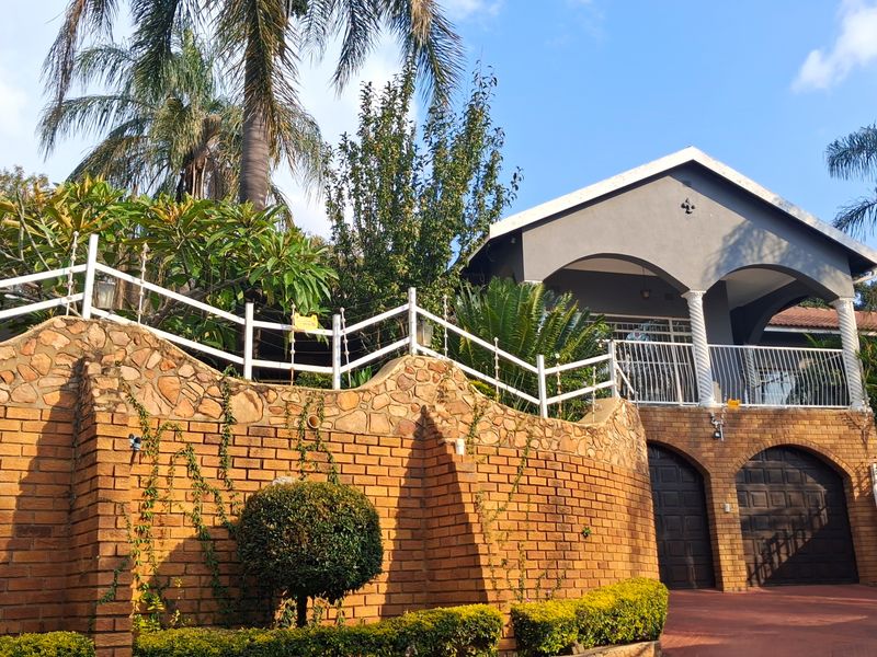 Front elevation of a multi-level house featuring a prominent brick retaining wall, arched garage doors, and an elevated balcony with decorative columns.
