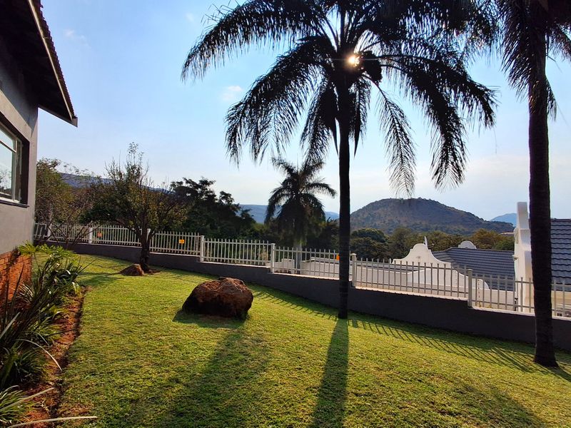 A well-maintained garden area featuring a manicured lawn, perimeter fencing, and scenic mountain views.