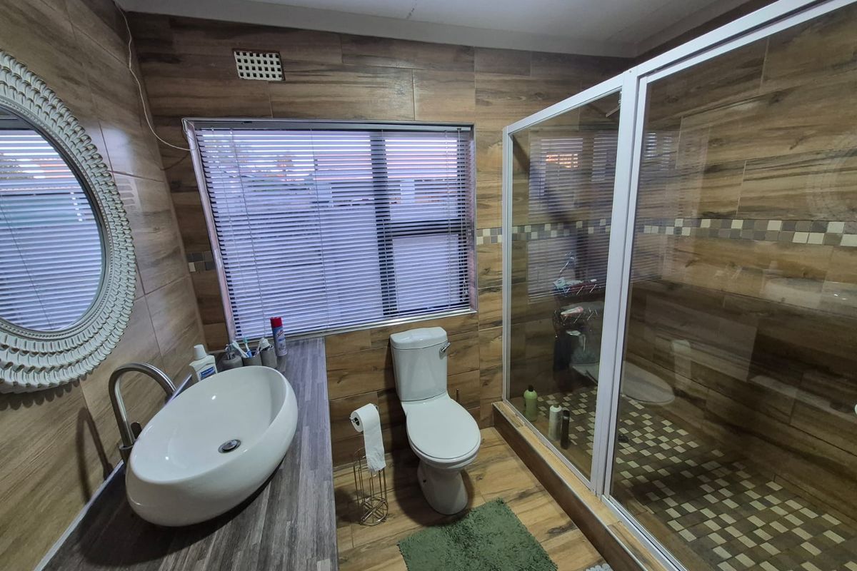 A modern bathroom featuring wood-look wall tiles, a vessel sink vanity, a toilet, and a glass-enclosed shower with mosaic floor tiling.