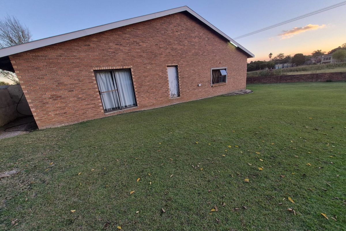 A view of the rear brick facade of the house, featuring a spacious lawn and established garden area.