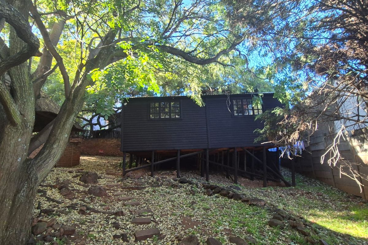 A stilted timber structure set within a natural garden area, featuring dark exterior cladding and grid-style windows.
