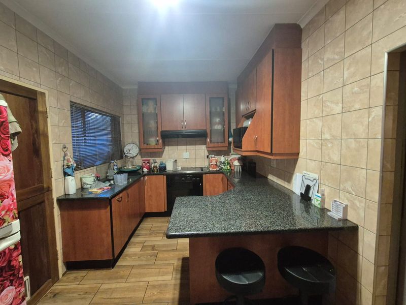 A functional kitchen featuring granite countertops, wood-finish cabinetry, a breakfast bar, and full-height ceramic wall tiling.