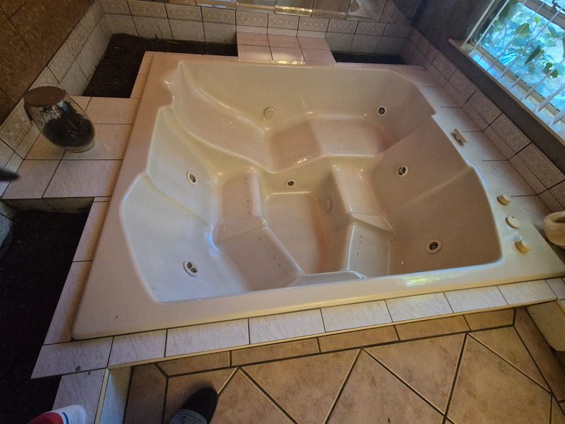 A bathroom featuring a large built-in spa bath with tiled surround, requiring maintenance to the surrounding tile work and finishings.
