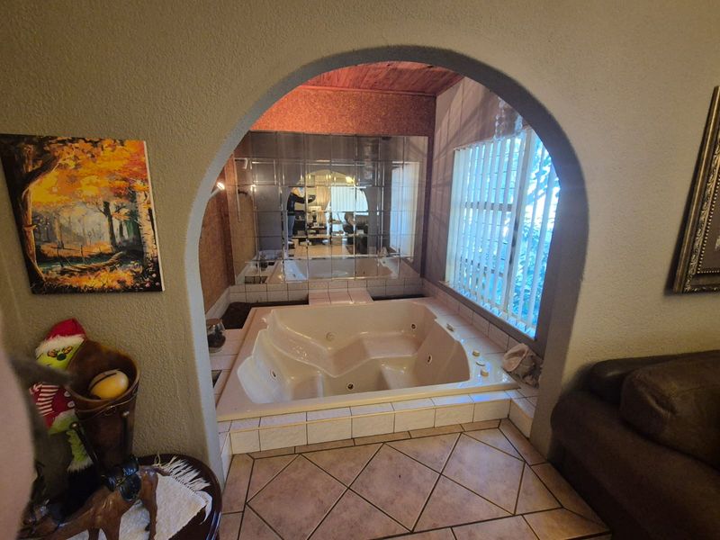 Bathroom featuring a built-in jetted bathtub set within an arched alcove, complemented by a mirrored wall and tiled flooring.