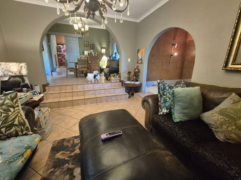 Open plan living area featuring tiled flooring, distinctive arched doorways, and a raised platform leading to an adjacent dining space.